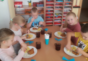 Dzieci przy stole podczas drugiego dania, skupione na czynności krojenia kotleta.